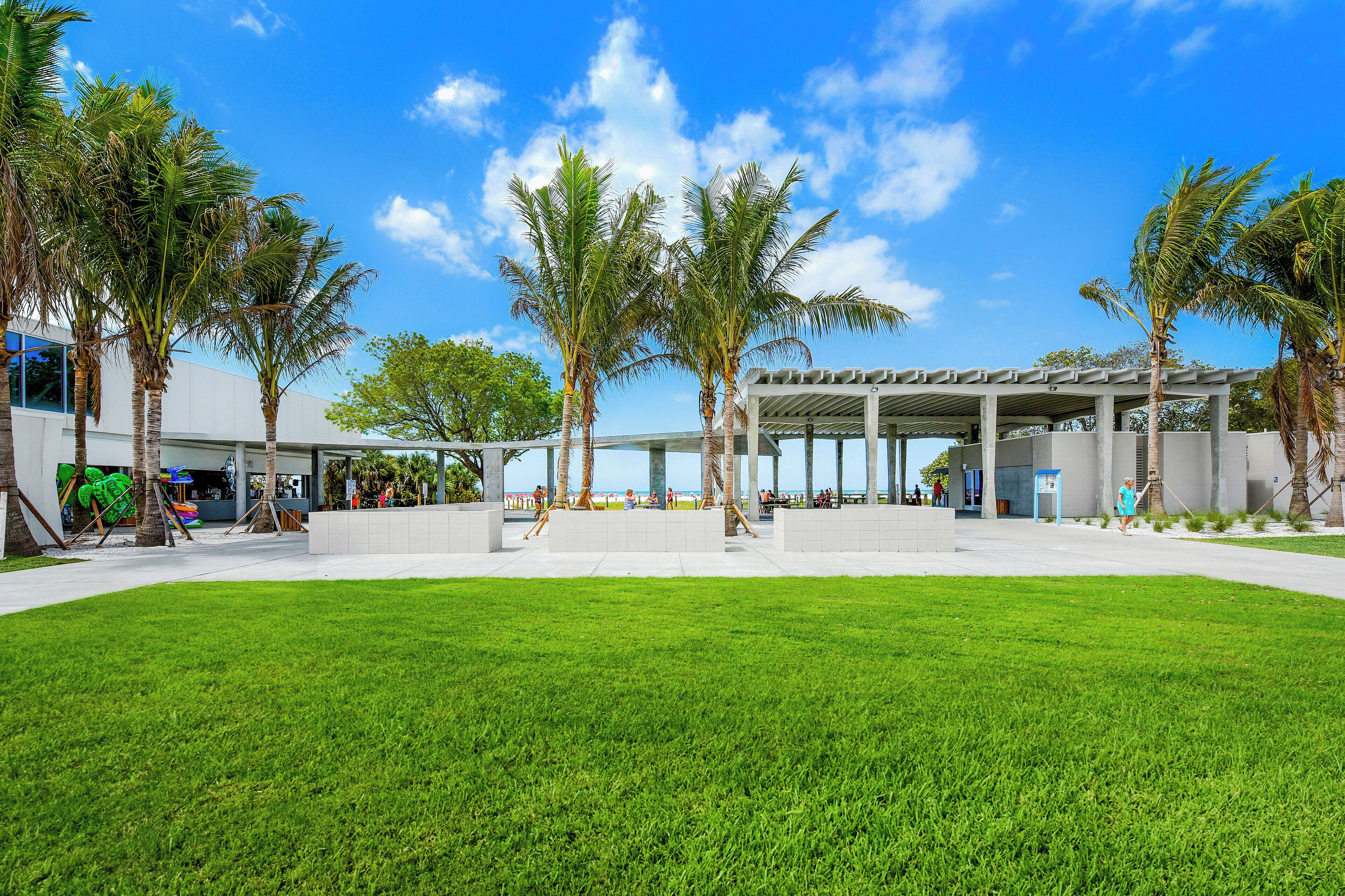 A modern building with a covered outdoor area, palm trees, and a well-maintained lawn.