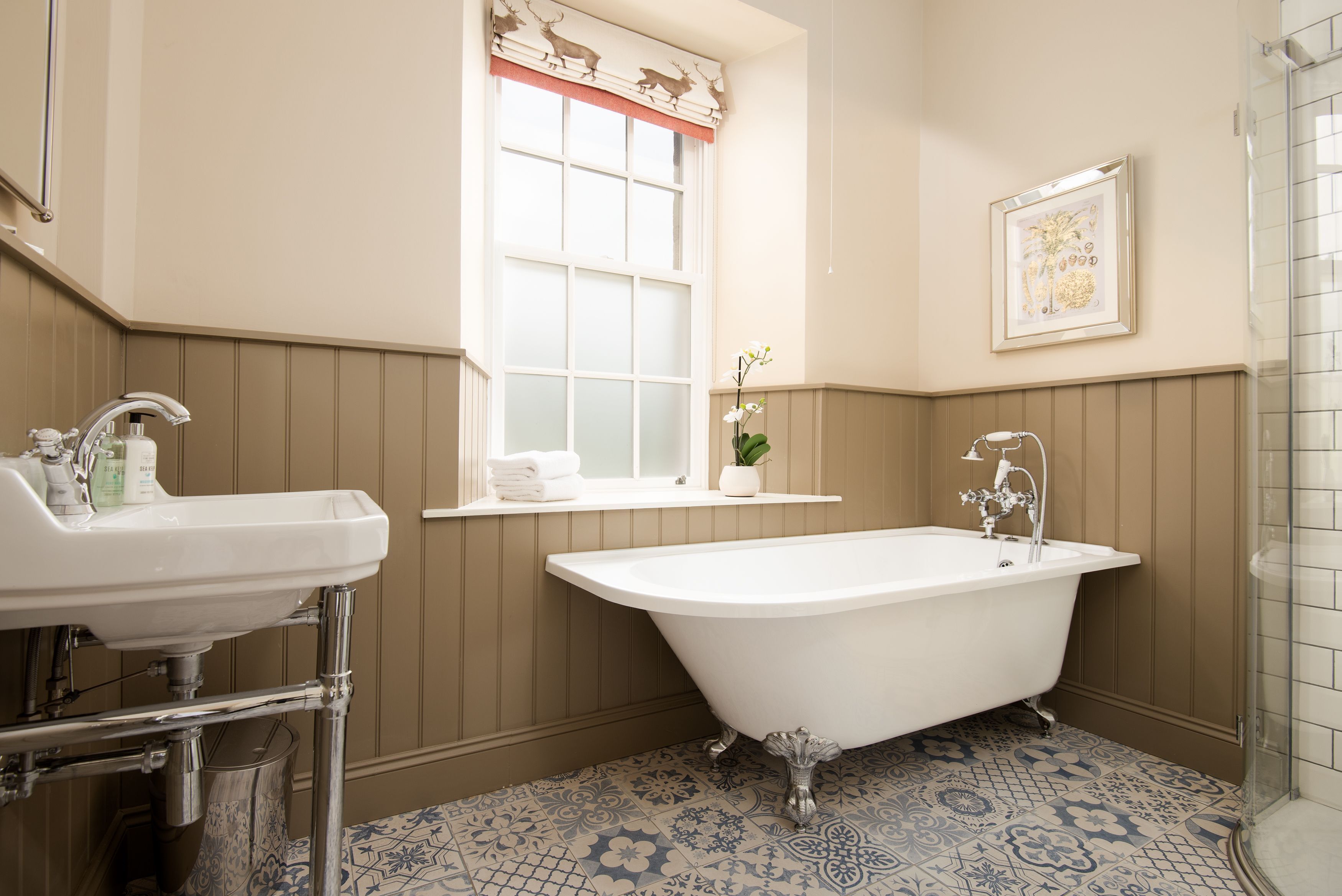 A bathroom with a freestanding bathtub, a sink, and a window with a decorative valance.