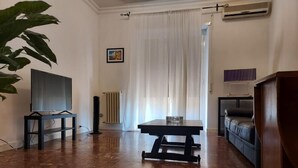 A living room with a dark brown tiled floor, a black table, a black sofa, a TV on a stand, and a radiator. - Direct connection to the city center. Comfortable apartment in the green. (Roma)