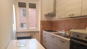 A compact kitchen with a white countertop, a gas stove, a built-in oven, and a window with a view of a building outside. - Direct connection to the city center. Comfortable apartment in the green. (Roma)
