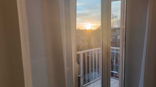 A balcony with a view of a sunset and buildings in the distance. - Direct connection to the city center. Comfortable apartment in the green. (Roma)