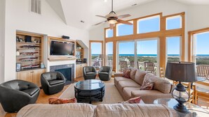A spacious living room with a large TV, comfortable seating, and a view of the ocean. - A Raye Of Sunshine: Ocean Views, Saltwater Pool (Corolla)