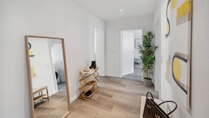 A modern hallway with a wooden floor, a mirror, a shoe rack, and a potted plant. - Business Flat in Little Tokyo (Düsseldorf)