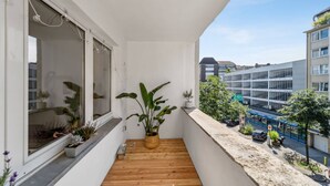 A balcony with wooden flooring, potted plants, and a view of a cityscape with buildings and a bus stop. - Business Flat in Little Tokyo (Düsseldorf)