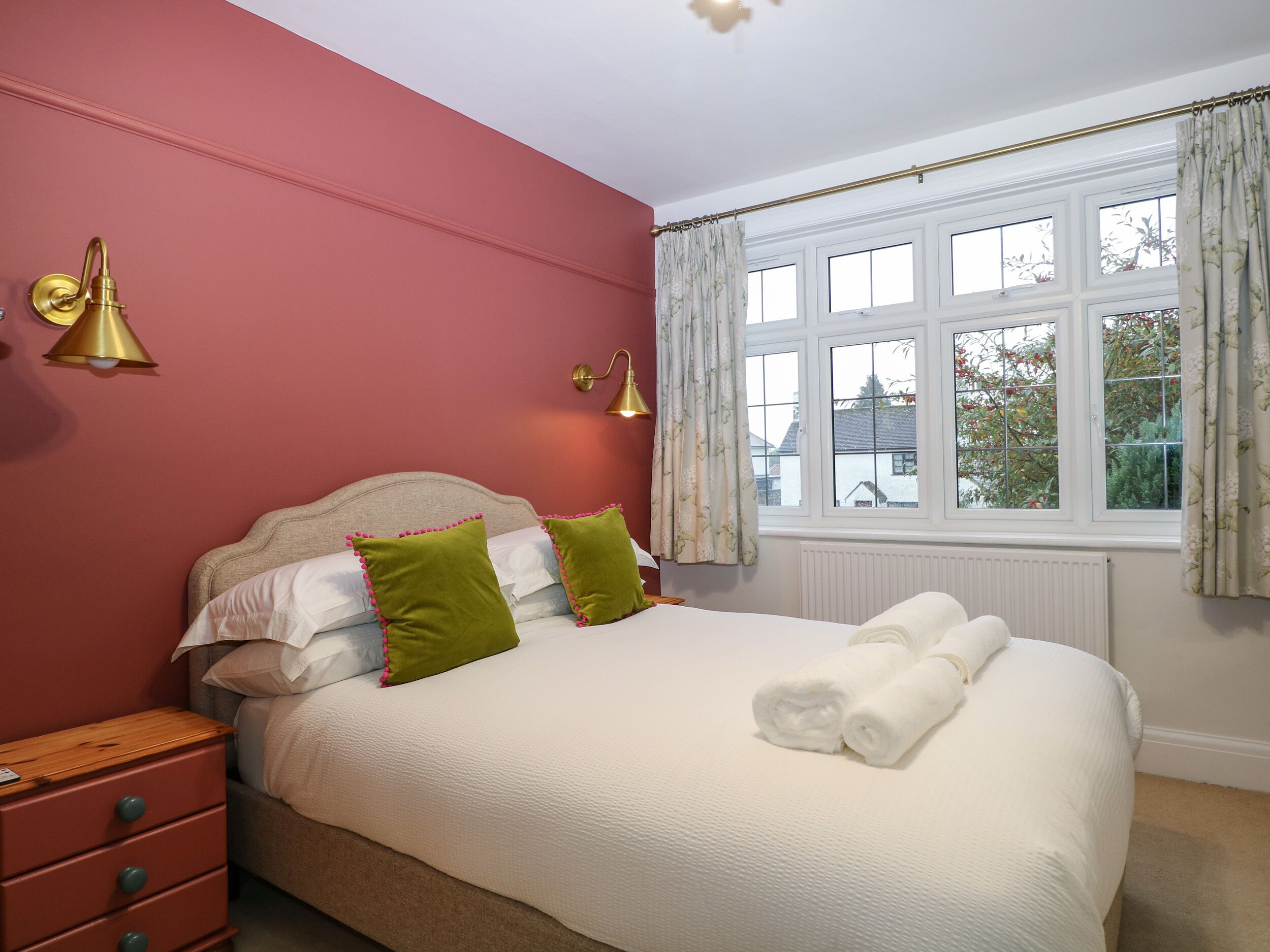 A neatly made bed with pillows, a bedside table with a lamp, and a window with curtains.