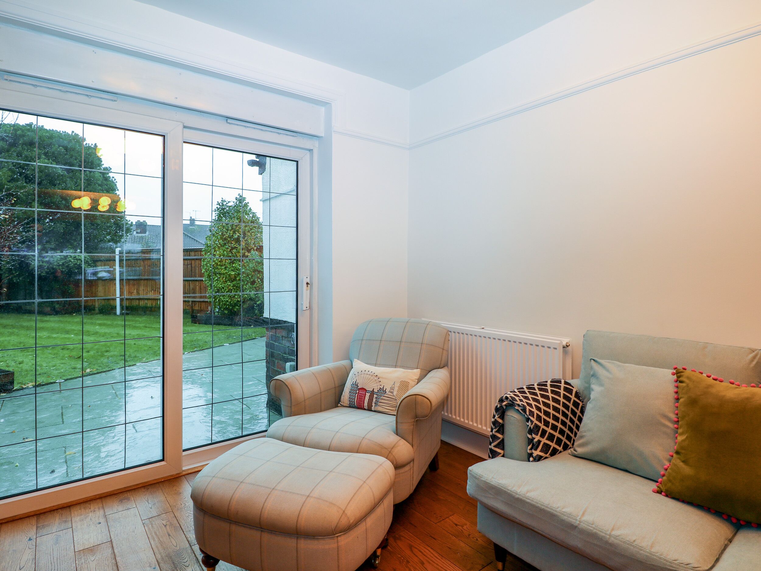 A living room with a large sliding glass door leading to a backyard, a sofa, and an ottoman.