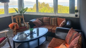 Un coin salon accueillant avec une table basse en verre, une chaise en bois et un canapé agrémenté de coussins à motifs.