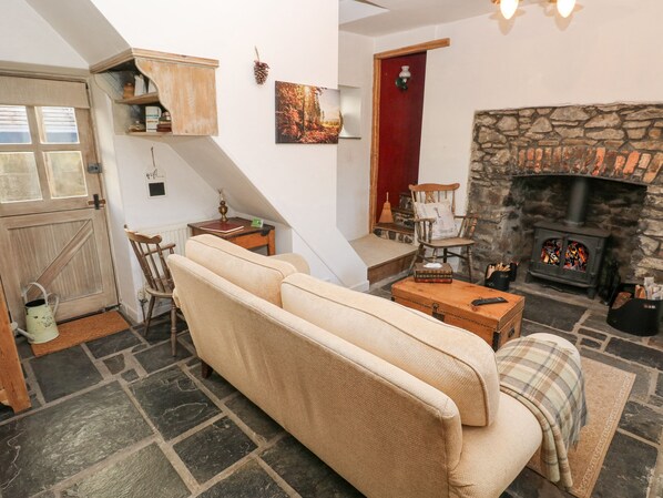 A cozy living room with a stone fireplace, a sofa, a wooden chest, and a staircase leading to another room.
