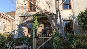 Un bâtiment en pierre avec une porte en bois, une chaise en métal et une plante en pot.
