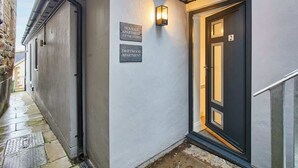 Une ruelle étroite mène à un immeuble doté de deux portes, chacune étant marquée d’un numéro et portant l’inscription « Appartement Sea Salt » et « Appartement Driftwood ».