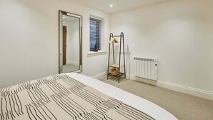 Une chambre à coucher avec un lit, un miroir, un radiateur et une fenêtre avec des stores.