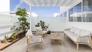Eine moderne Außenpatio mit einem weißen Sofa, Korbstühlen und einem Holztisch.