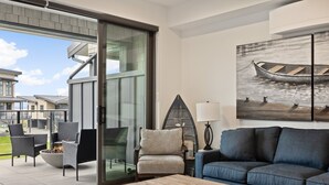 Una sala de estar moderna con un sofá azul, una mesa de centro de madera y un ventanal que da a un patio exterior con sillas y una chimenea.