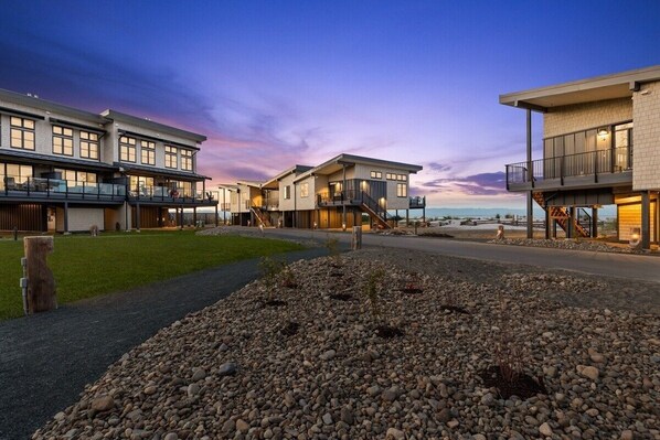 A modern residential building with multiple balconies, a well-maintained garden, and a view of the ocean.