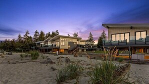 Una propiedad moderna frente a la playa con un amplio espacio exterior, una terraza cubierta y una habitación espaciosa con grandes ventanales.