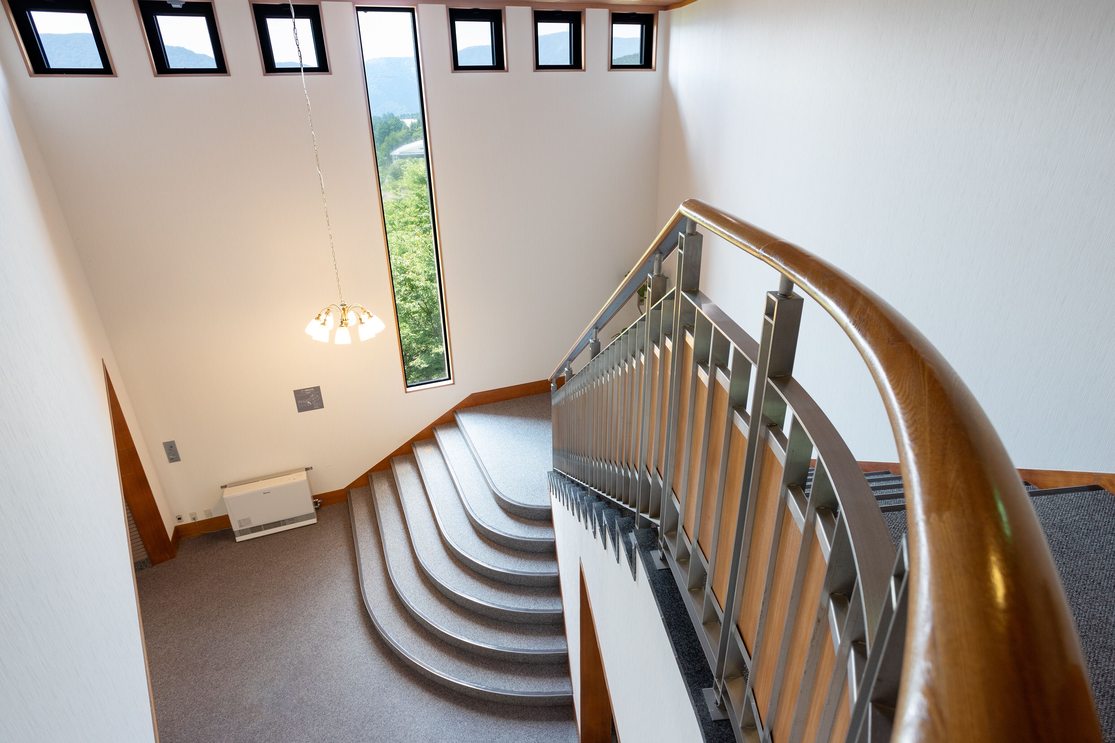 A modern staircase with a metal railing, carpeted steps, and a view of greenery outside through a large window.