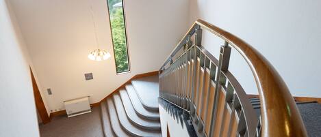 A modern staircase with a metal railing, carpeted steps, and a view of greenery outside through a large window.