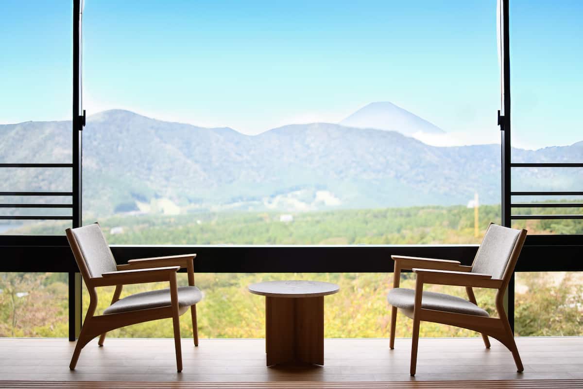 Ein Zimmer mit zwei Holzstühlen und einem kleinen runden Tisch, große Fenster mit Blick auf die Berge.