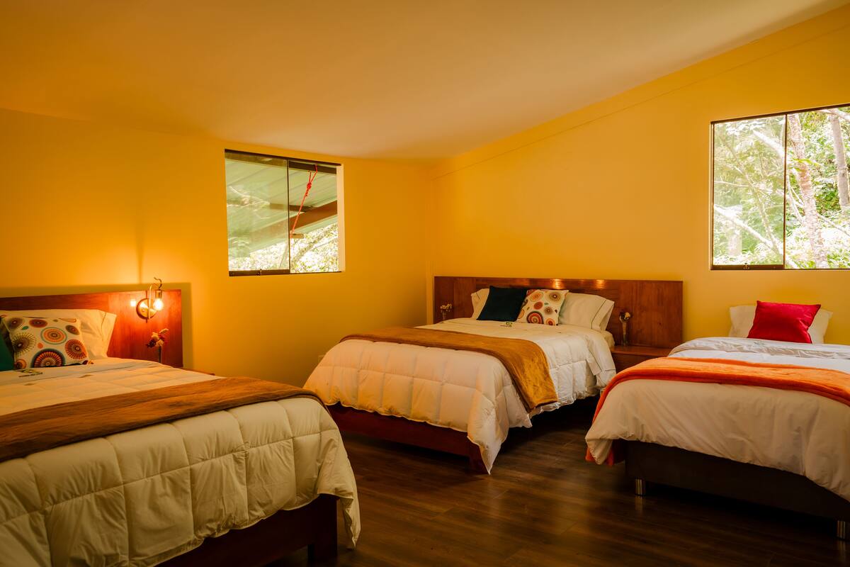A hotel room with three beds, wooden flooring, and large windows with natural light.
