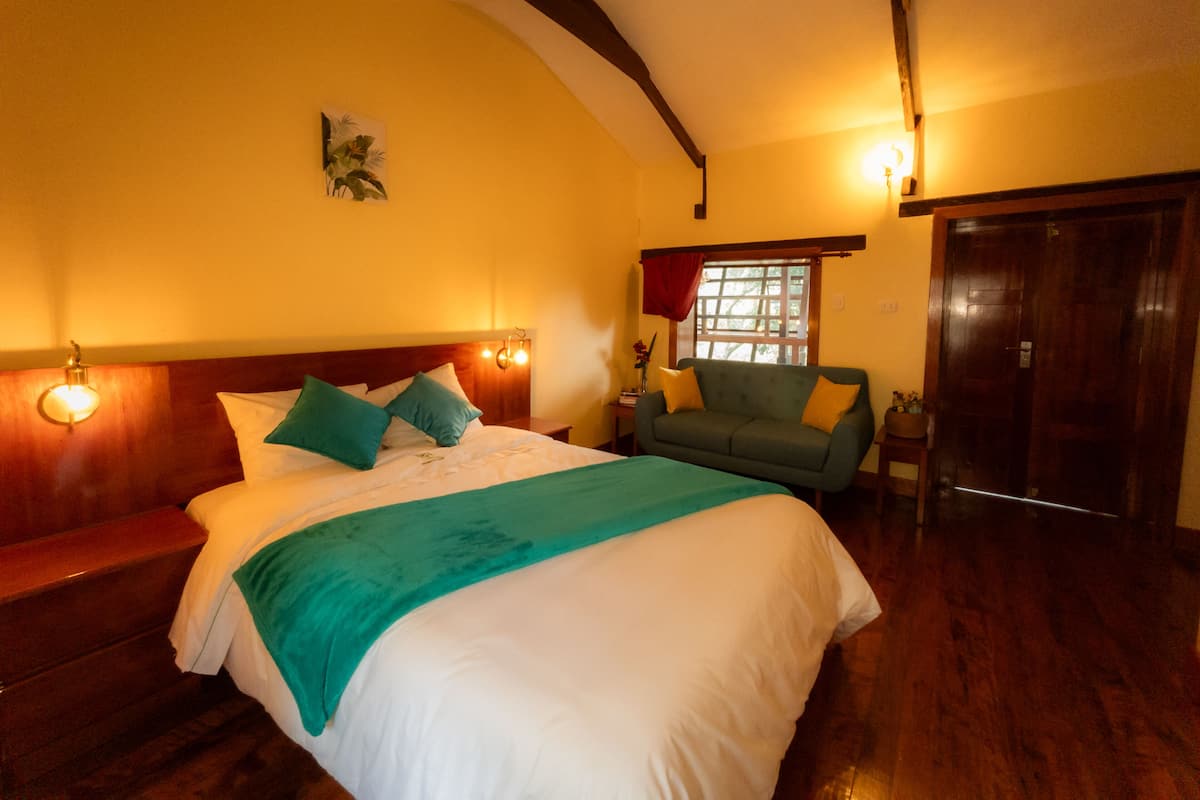 A bedroom with a large bed, a wooden headboard, a green sofa, a wooden door, and a window with a red curtain.