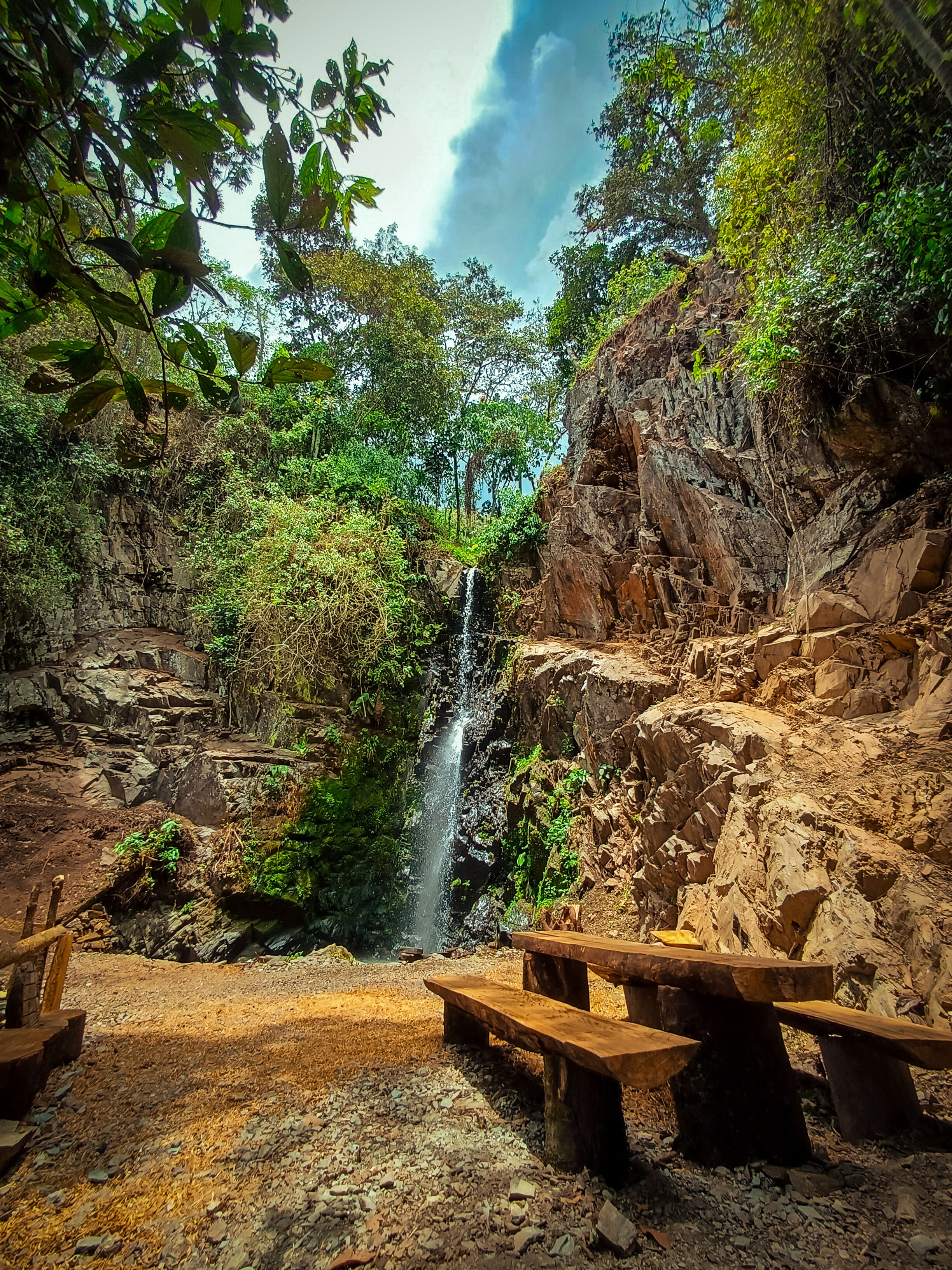 Un entorno natural con cascada, terreno rocoso y mesas de picnic.