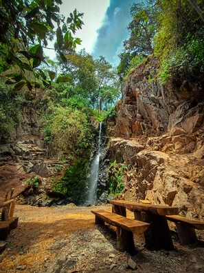 A natural setting with a waterfall, rocky terrain, and picnic tables. - Ecoterra Inka Lodge (Santa Ana)
