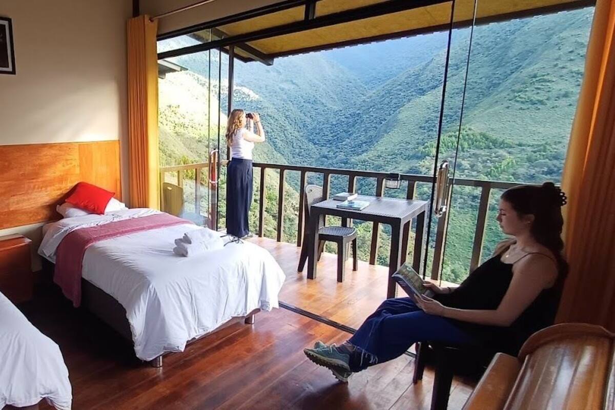 A hotel room with two beds, a balcony, and a view of a mountainous landscape.