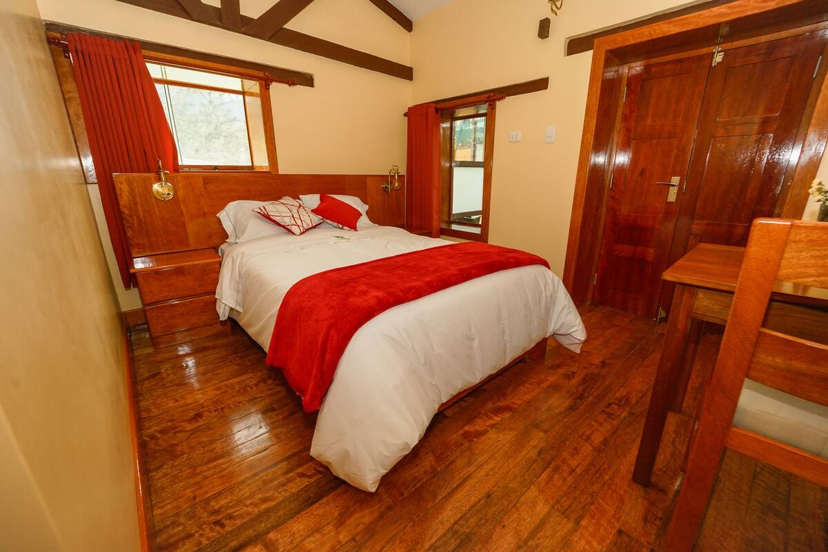 A bedroom with a wooden bed, red curtains, and a wooden wardrobe.