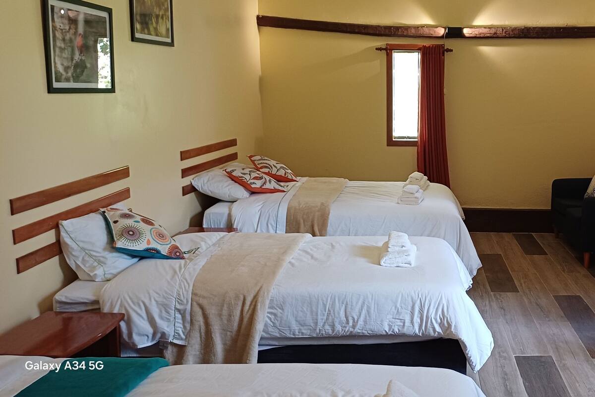 A hotel room with two beds, a chair, a small table, a mirror, and a staircase.