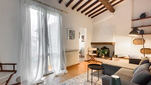 Sala de estar com sofá, mesa de centro, abajur e vista para o exterior através de cortinas leves.