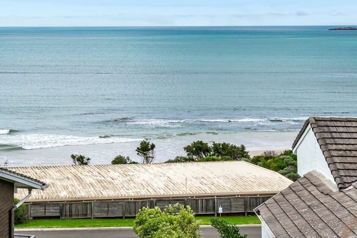 A coastal view with a beach, a building with a corrugated metal roof, and a clear sky.