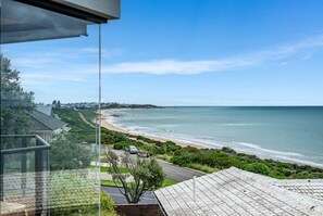 Vista sulla costa da un balcone che si affaccia su una spiaggia, una strada e edifici residenziali.