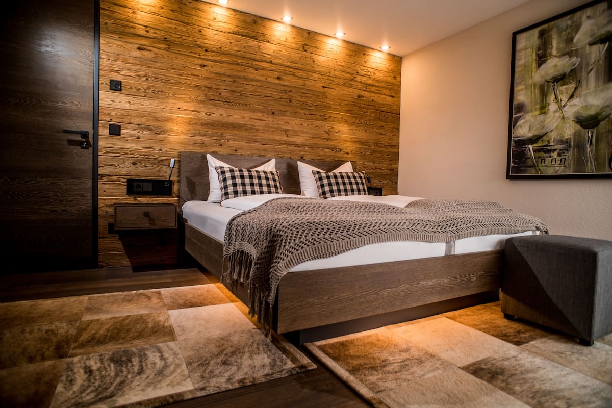 Een moderne slaapkamer met een houten hoofdbord, een bed met een gebloemd deken, een nachtkastje en een bijzettafeltje met een lamp.