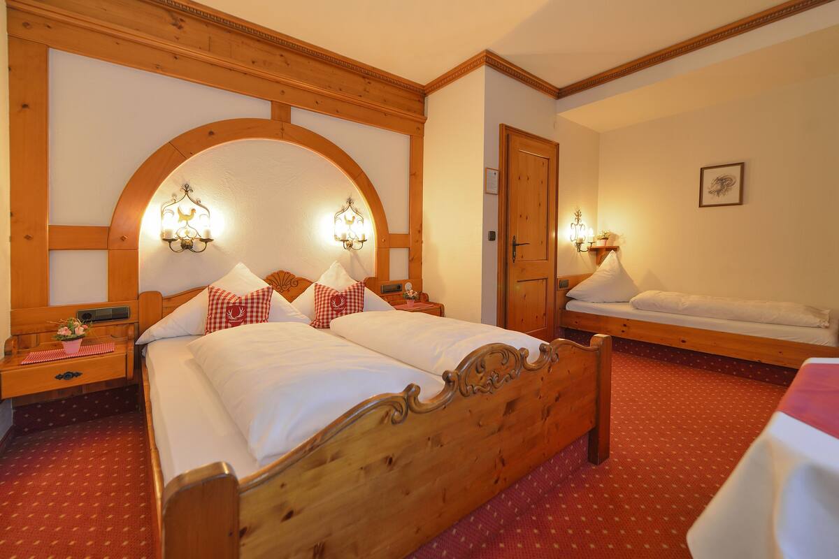 Hotelkamer met een groot bed, een kleiner bed, een houten hoofdbord, twee nachtkastjes met lampen, een deur en een klein wandplankje.