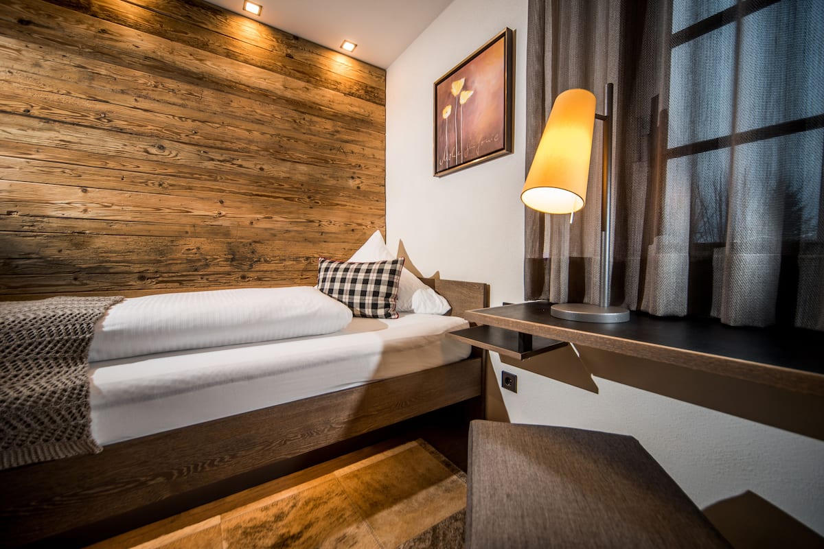 Een moderne hotelkamer met een houten wand, een bed met witte lakens, een nachtkastje met lamp en een raam met gordijnen.