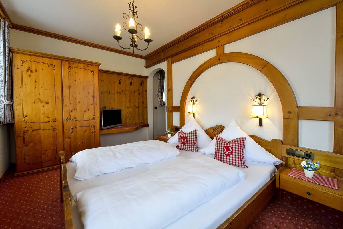Een hotelkamer met een houten bed, een televisie, een houten kledingkast en een kroonluchter.