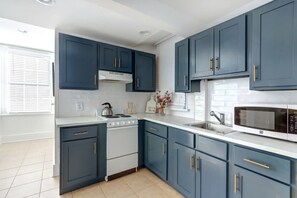 A modern kitchen with dark blue cabinets, white countertops, a stove, a microwave, and a sink.