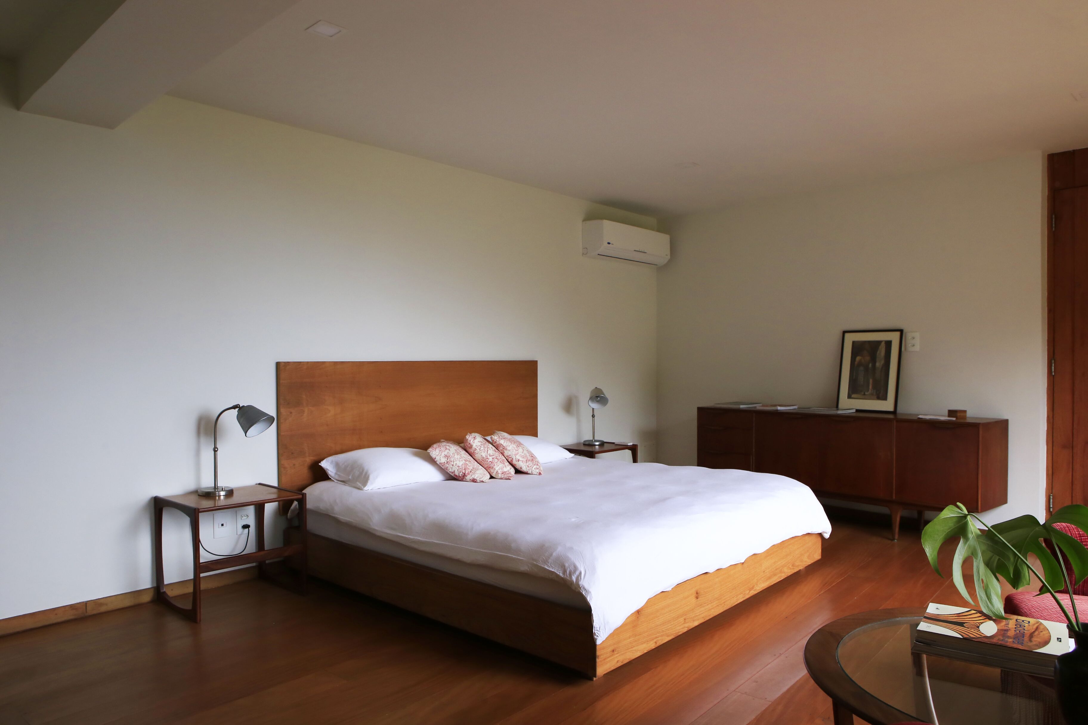 A bedroom with a wooden bed, bedside tables, a nightstand, a wooden dresser, and a potted plant.