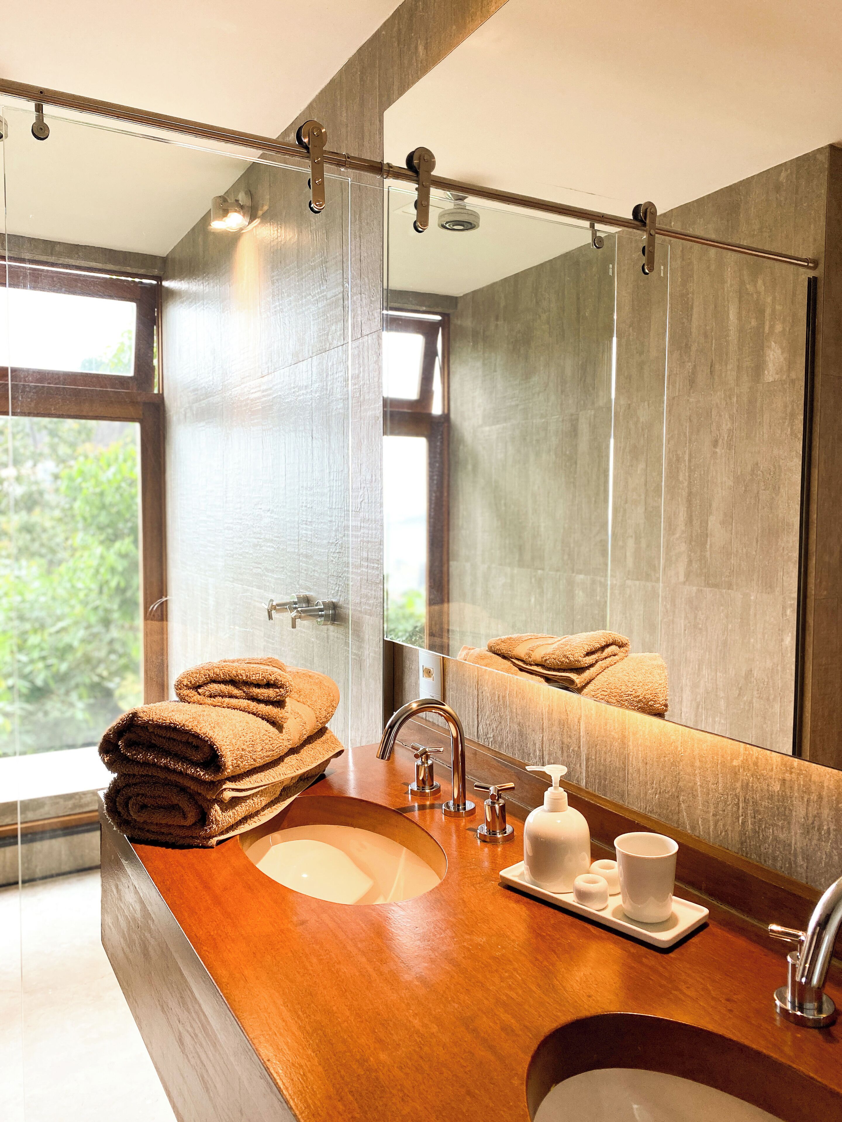 A modern bathroom with a wooden vanity, two sinks, a large mirror, and towels.