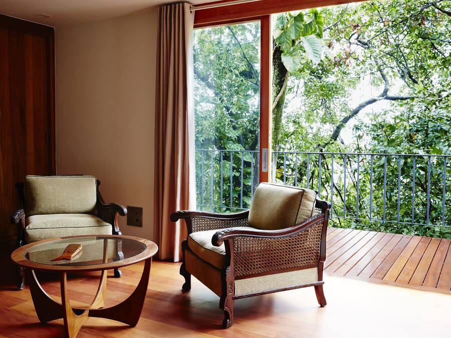 Una habitación con dos sillas, una mesa de centro de vidrio y un ventanal con vistas a árboles.