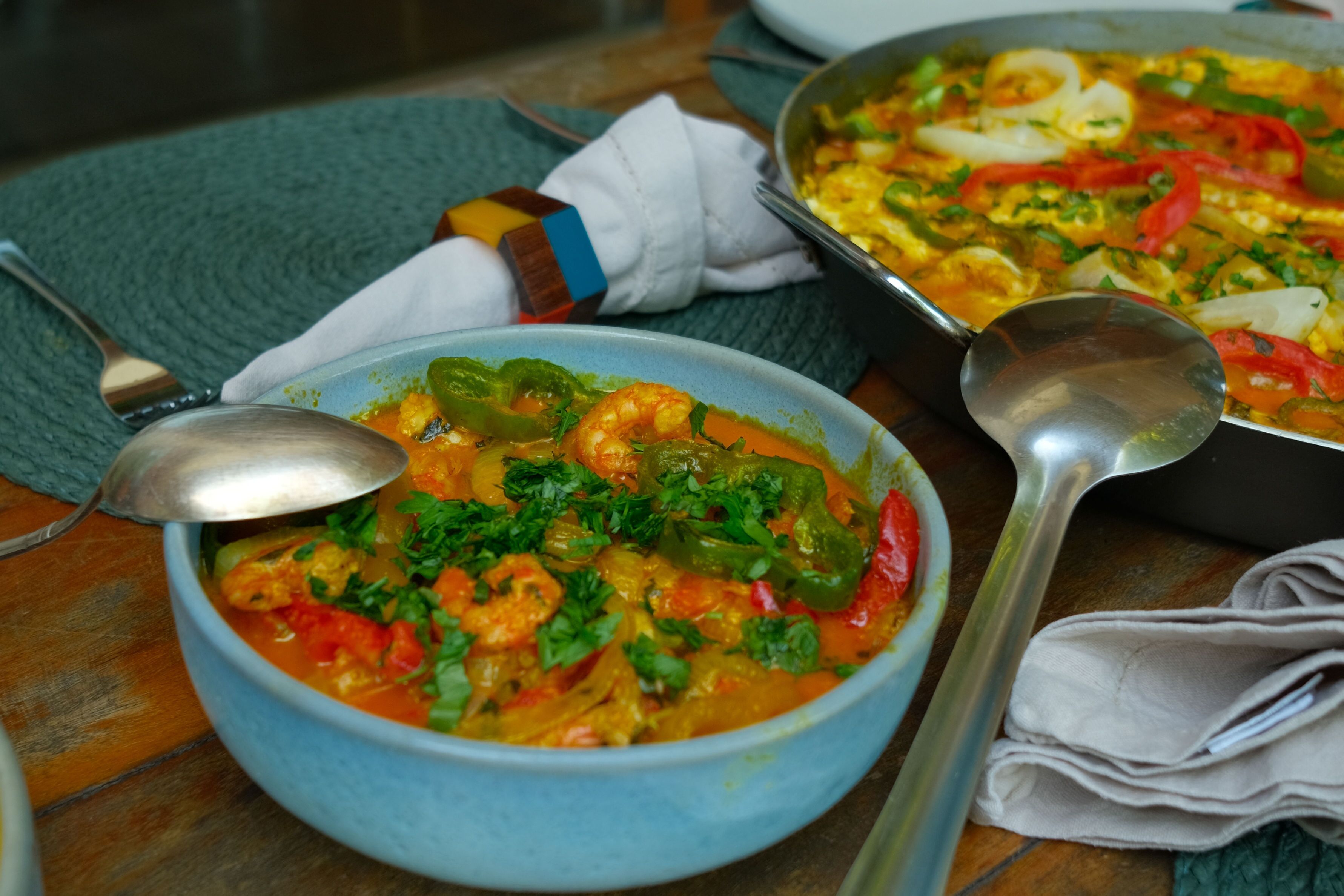 A bowl of seafood stew with a spoon and a ladle on a table.