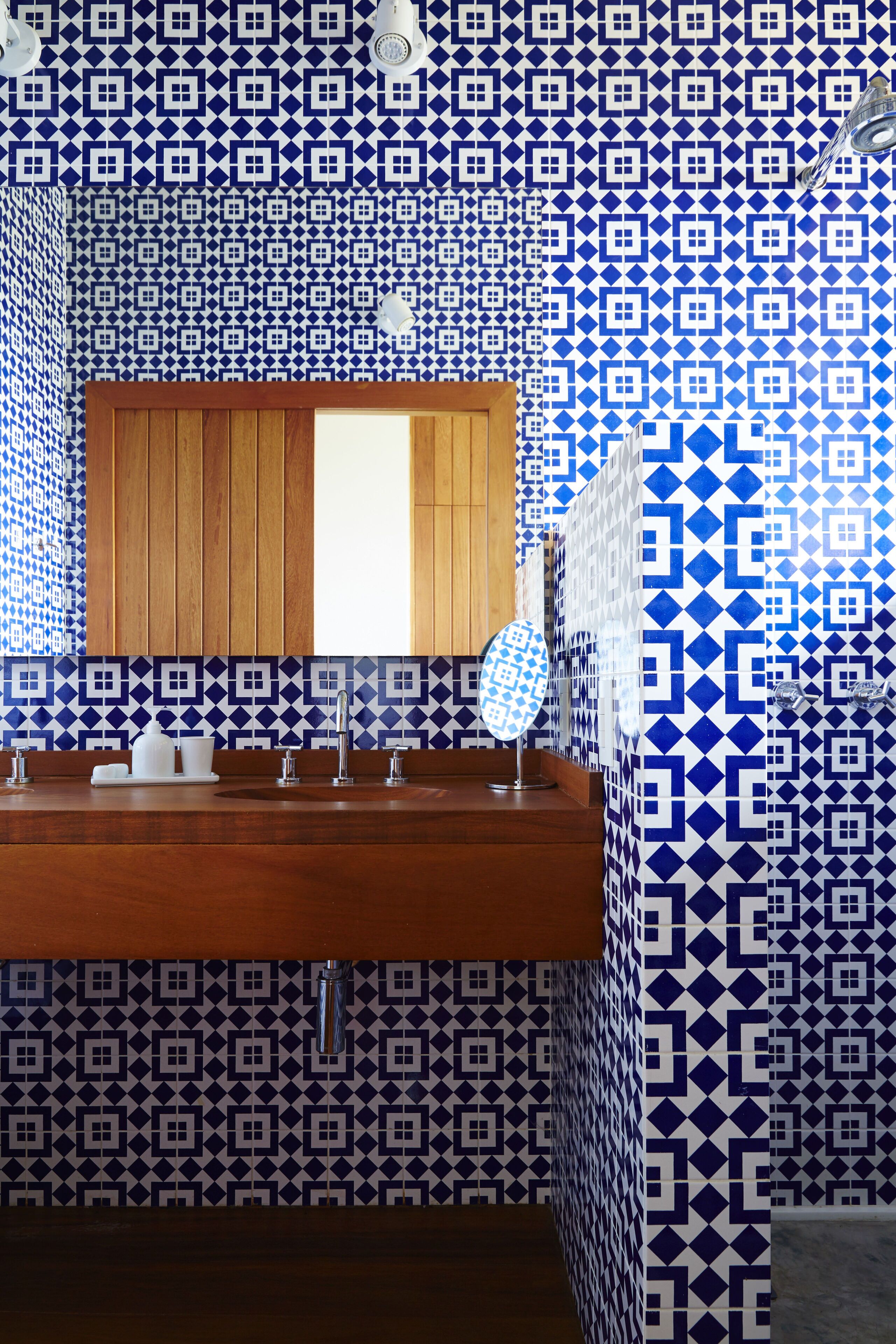 A bathroom with a wooden vanity, a mirror, and a patterned blue and white tile backsplash.