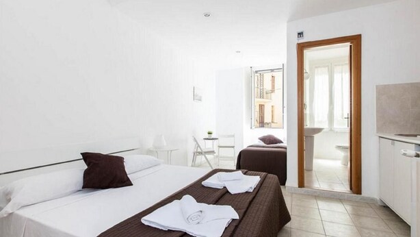 A hotel room with two beds, a small table, and a bathroom visible through an open door. - A room close to Colosseum (Roma)