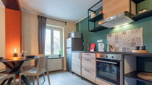 Una cucina moderna con zona pranzo, dotata di forno a incasso, frigorifero e finestra con tende.