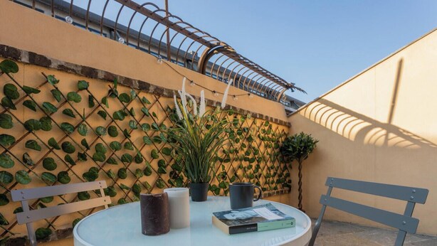 Un tavolo rotondo con sedie, un vaso con una pianta e un libro, il tutto davanti a un muro con una pianta rampicante.