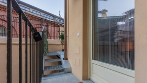 Una stretta scala esterna conduce a una porta con cancello in metallo e un piccolo vaso con una pianta.
