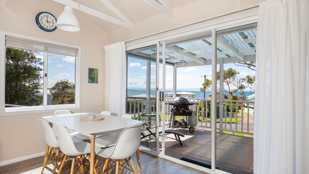 Een eetruimte met een tafel en stoelen, een grill buiten en uitzicht op zee.