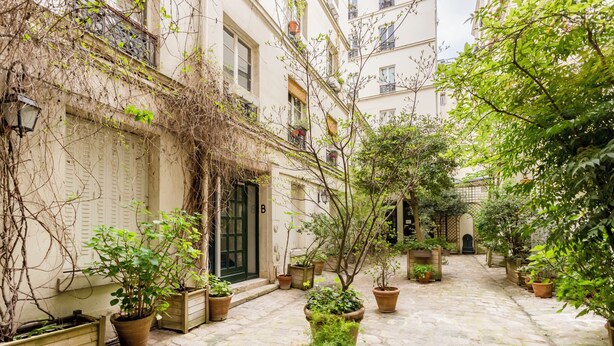 A courtyard with potted plants, a cobblestone path, and a building with a green door. - Sévigné le Marais Place des Vosges (Paris)
