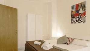 A hotel room with a bed, a wooden door, a white wardrobe, and a painting on the wall. - Studio 3 at the Colosseum (Roma)