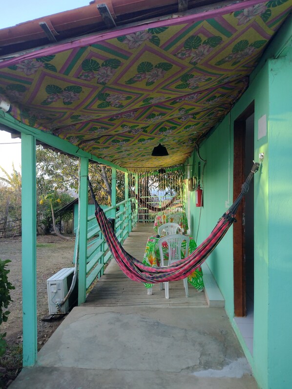 A covered outdoor area with a hammock, chairs, and a pathway leading to a building entrance. - Palhoça da Colina (Fernando de Noronha)